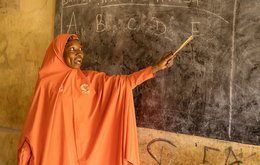 A woman points to a blackboard with the letters A B C D E on it