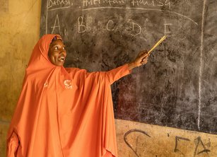 A woman points to a blackboard with the letters A B C D E on it