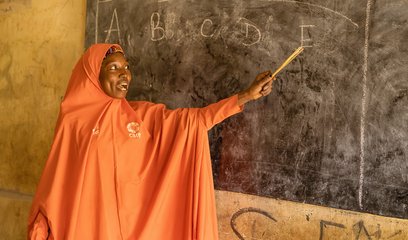 A woman points to a blackboard with the letters A B C D E on it