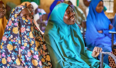 Two women in a classroom setting (other women are visible in the background)