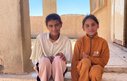 Two young girls sit together on the steps of a stone building