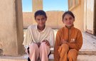Two young girls sit together on the steps of a stone building
