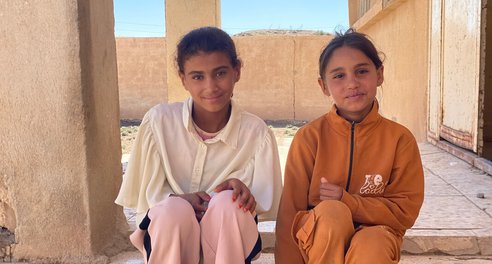Two young girls sit together on the steps of a stone building