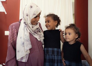 A woman and two young girls smile at each other in a hospital clinic room