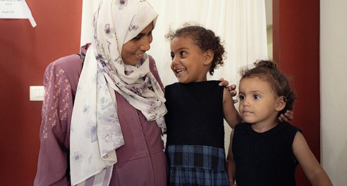 A woman and two young girls smile at each other in a hospital clinic room