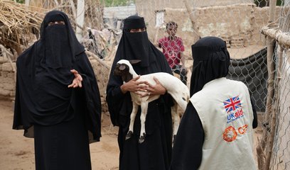 Two women talk to another woman in a CARE vest. One of the women is holding a goat.