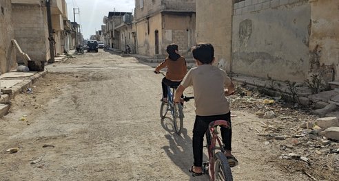 Children cycle through destroyed neighbourhoods in Syria