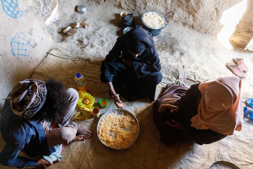 An aerial view of three women sat on the floor gathered round a simple meal