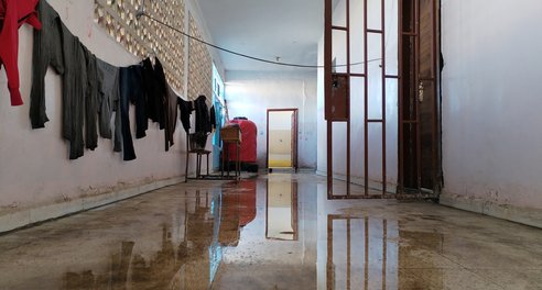 A flooded, bare hallway with clothes hanging up along the wall