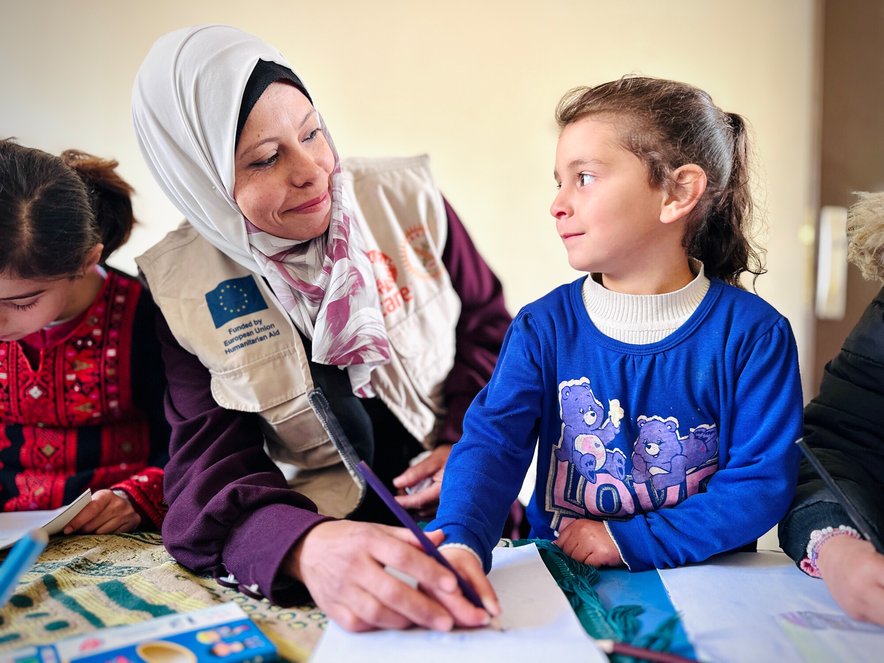 A woman and young girl sit together at a table with pencil and paper