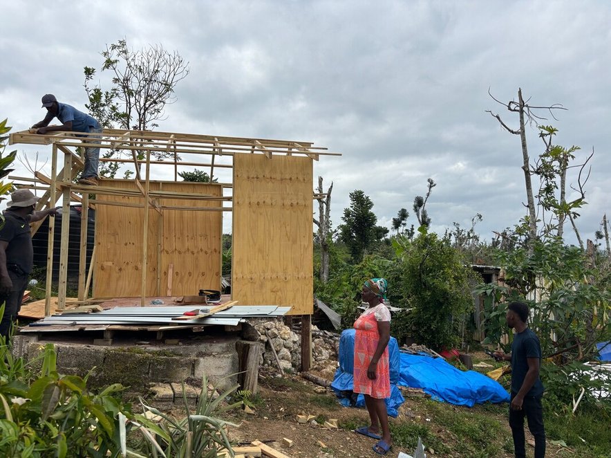 A woman looks at the wooden structure of a temporary shelter under construction