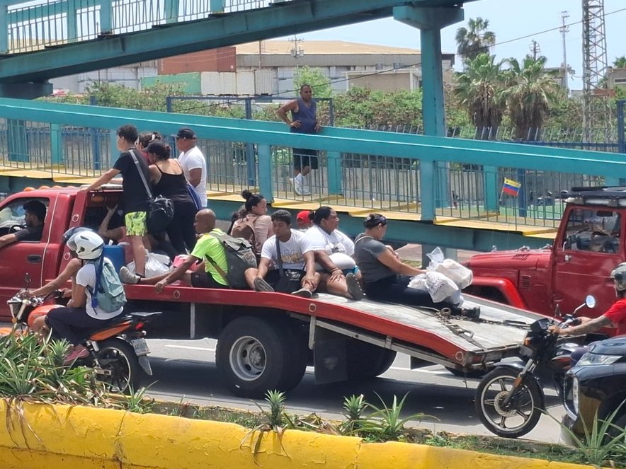 A group of about 10 people sit in traffic on the back of a pick up truck