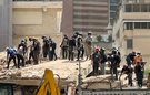 About 25 rescue workers, most wearing hard hats, working through the rubble of a collapsed building