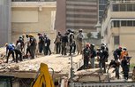 About 25 rescue workers, most wearing hard hats, working through the rubble of a collapsed building