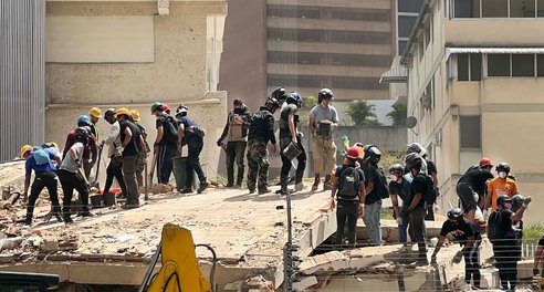 About 25 rescue workers, most wearing hard hats, working through the rubble of a collapsed building