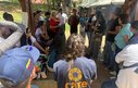 A woman in a CARE vest talks with a group of aid workers and earthquake survivors. Temporary shelters are visible in the background