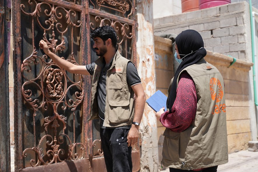 Two healthworkers wearing CARE vest knock on a door