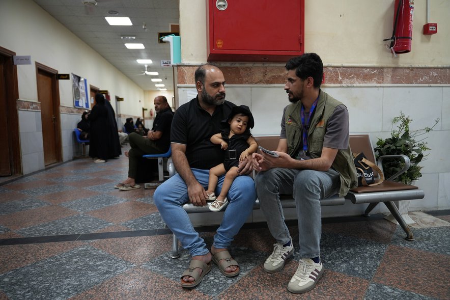 A healthworker speaks to a man holding a child in a hospital waiting room