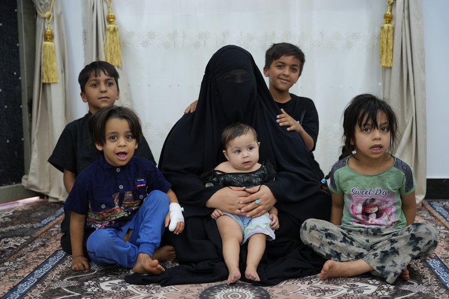 A woman in a hijab sits with 5 young children