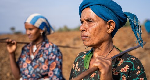 Two women carry their tools as they prepare to work farmland in Ethiopia