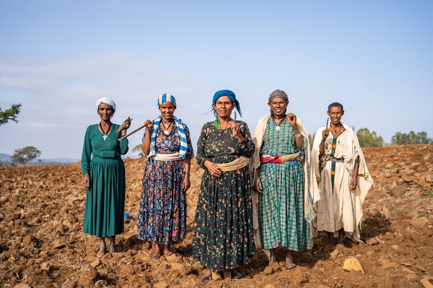 A group of 5 women stand looking confidently to camera in a field that looks like it has been recently ploughed