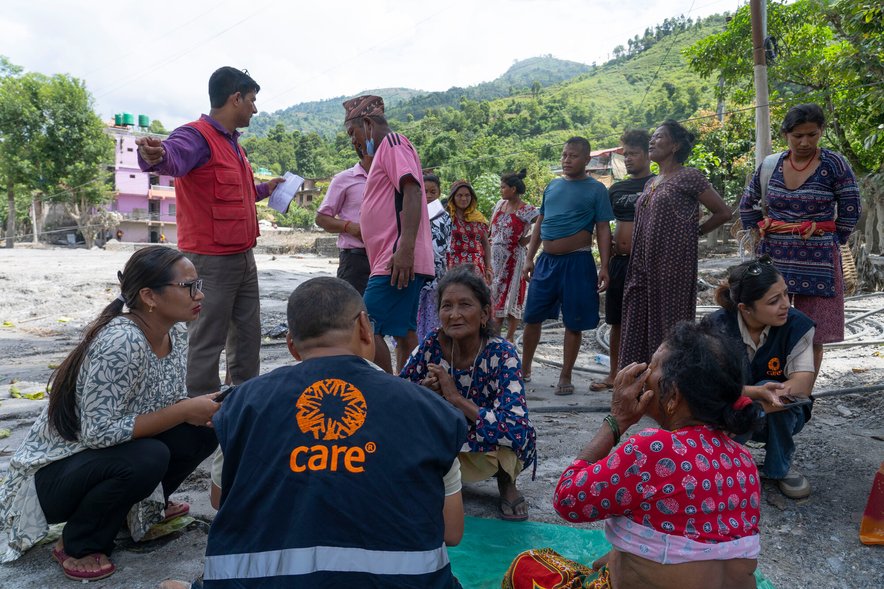 CARE staff sit talking with women flood survivors. Several other survivors are visible in the background.