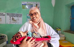 A female health professional cradles a newborn baby in her arms in a hospital setting