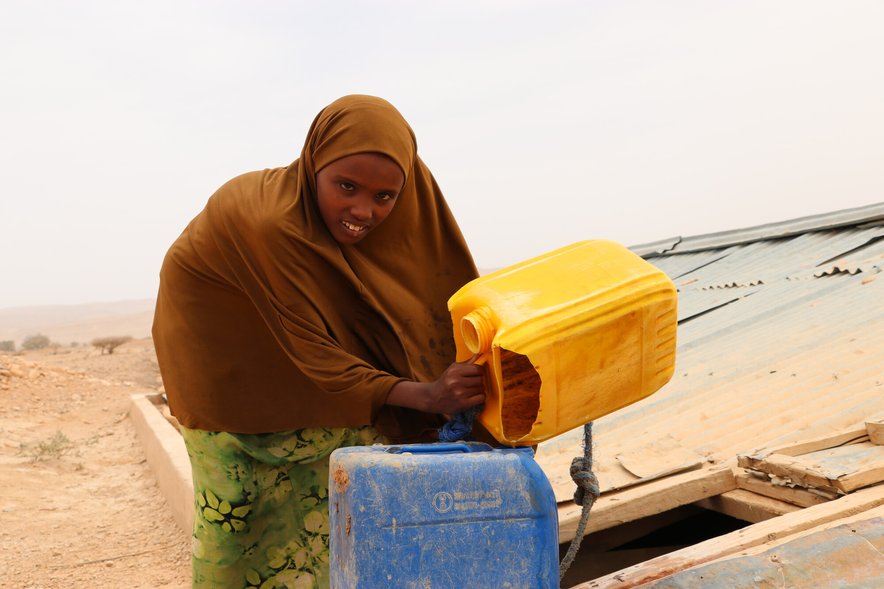 A young girl filling up a water container in a remote and arid landscape