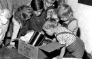 A black and white image of six young children leaning over a cardbox box full of food