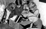 A black and white image of six young children leaning over a cardbox box full of food