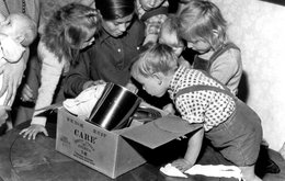 A black and white image of six young children leaning over a cardbox box full of food