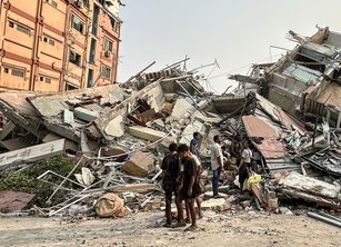 A group of people standing in front of a large pile of rubble from buildings destroyed by the earthquakes