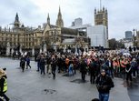 A large group of people march outside UK Parliament; Many are holding placards with the slogan 'March4Women'