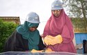 Two young women wearing hard hats leaning over a solar panel