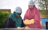 Two young women wearing hard hats leaning over a solar panel