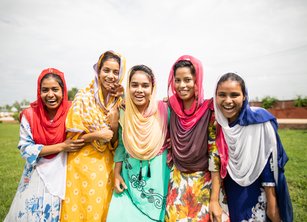 A group of five women stand together outside smiling and laughing