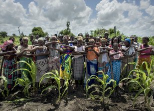 A large group of women in a field, making the equals sign with their arms