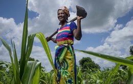 A woman stands holding a large spade in a field