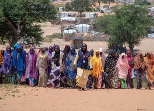 A line of women walk together up a dusty hill
