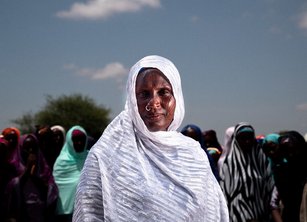 A woman wearing a white headscarf stands proudly in front of a large group of women