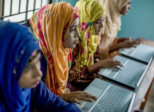 Four women sit in a row using laptops