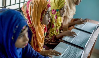 Four women sit in a row using laptops