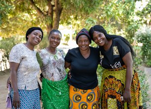 A group of four smiling women pose for the camera together underneath a tree