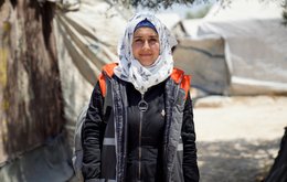An aid worker looks to camera, tents from a refugee camp are visible in the background