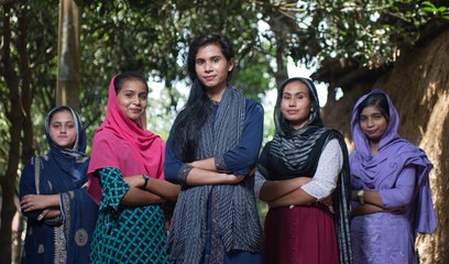 A group women stand with their arms folded in a triangle formation