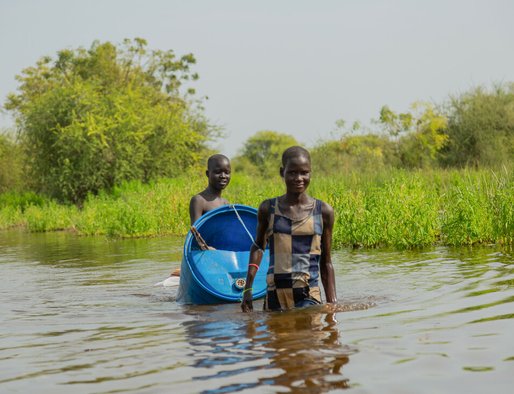 A young man and woman waist deep in flood waters, pulling a plastic container