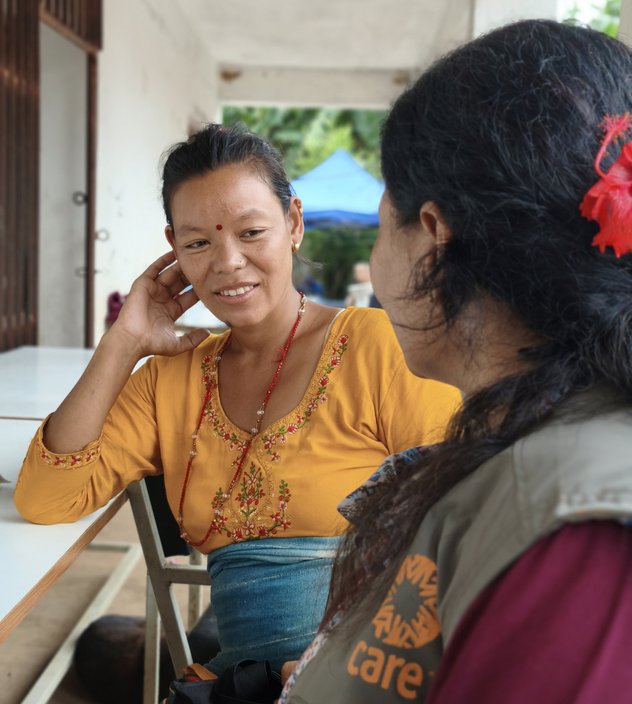 Two women in conversation. One of them is wearing a vest with the CARE logo.
