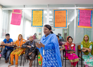 A woman speaking at a training session, with trainees listening in the background