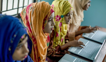 Four women sit in a row using laptops