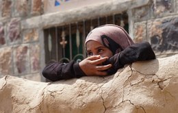 A young girl looks ahead of her, with her arms folded on a wall